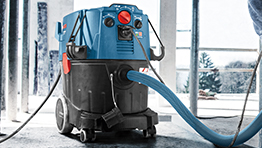 A blue Bosch Professional vacuum cleaner on a construction site with a hose attached.