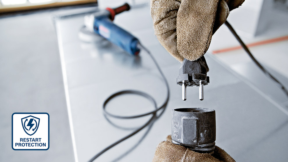 A gloved hand holds an electrical plug above a socket on a work surface.