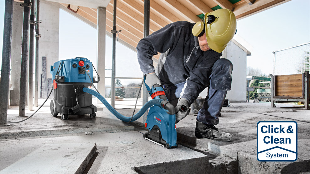 A worker in a helmet uses a Bosch tool on concrete at a construction site.