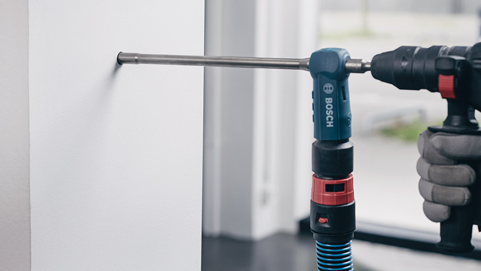 A Bosch Professional screwdriver is drilling into a white wall, hand gripping tool firmly.