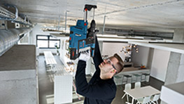 A man uses a blue Bosch Professional tool to work on a ceiling in a modern office space.